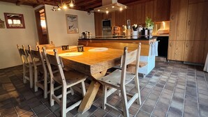 Ein Holzespeisesaal mit sechs Stühlen, ein Küchenbereich mit Holzschränken und ein Fliesenboden.