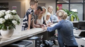 Een groep mensen in een modern kantoorpand met een receptiebalie, computers en een potplant.