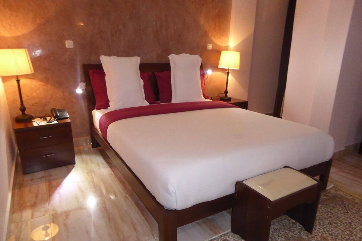 Quarto de hotel com uma cama grande, duas mesas de cabeceira e uma mesinha de apoio com telefone.