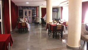 Tilava ravintola, jossa on useita pöytiä ja tuoleja, punaiset verhot ja laatoitettu lattia.