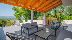 An outdoor patio with wooden ceiling, grey sofas, and a black chair. - Beautiful home in Glavina Donja (Glavina Donja)
