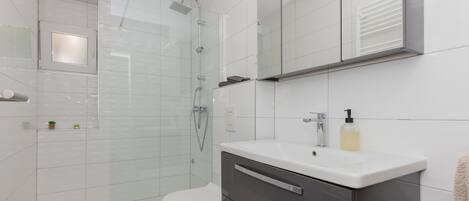A modern bathroom with a glass shower enclosure, a white toilet, a vanity with a mirror, and a small plant on the countertop.
