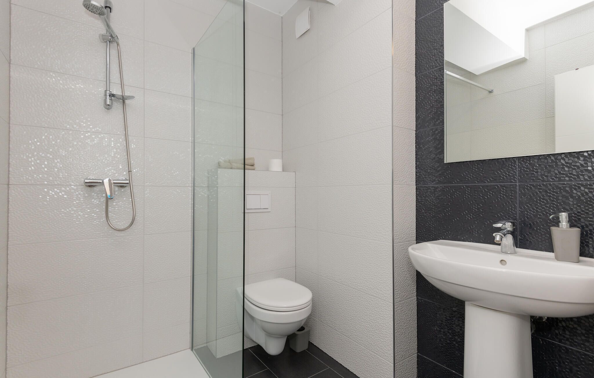 Een moderne badkamer met een douchecabine van glas, een toilet en een wastafel met een spiegel erboven.