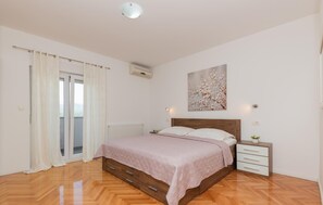 A bedroom with a wooden bed, a nightstand, a radiator, a window with curtains, and a ceiling light.