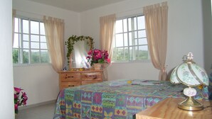 Une chambre à coucher avec un lit, une commode, une lampe et des fenêtres avec des rideaux.