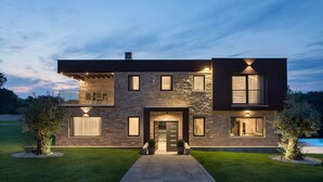 Una casa moderna de dos pisos con fachada de piedra, ventanas amplias y una entrada bien iluminada.