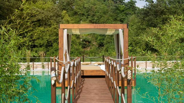 Un puente de madera con barandillas de cuerda que lleva a una plataforma sobre una piscina.