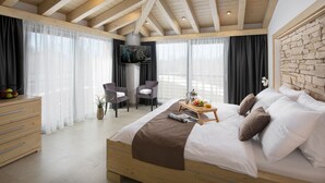 Un dormitorio moderno con techo de madera, una cama grande con ropa de cama blanca y marrón, una mesita de noche con frutas y un libro, y un televisor montado en la pared.