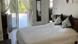 A bedroom with a bed, a dresser, a ceiling fan, a window with curtains, and a painting on the wall. - Villa With Private Pool And Stunning Sea Views And Large Landscaped Gardens (Peyia)