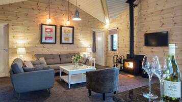 A cozy log cabin interior with a sofa, armchairs, a coffee table, a fireplace, and a wine bottle.