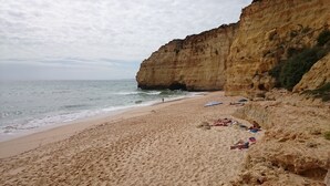 Une plage bordée d’une falaise rocheuse, avec un rivage sablonneux et une mer calme.