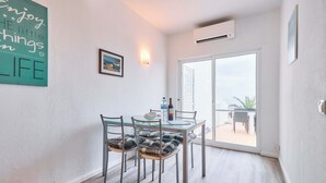 Un coin repas avec une table en verre et des chaises en métal, un climatiseur fixé au mur et une porte-fenêtre coulissante donnant sur une terrasse extérieure.