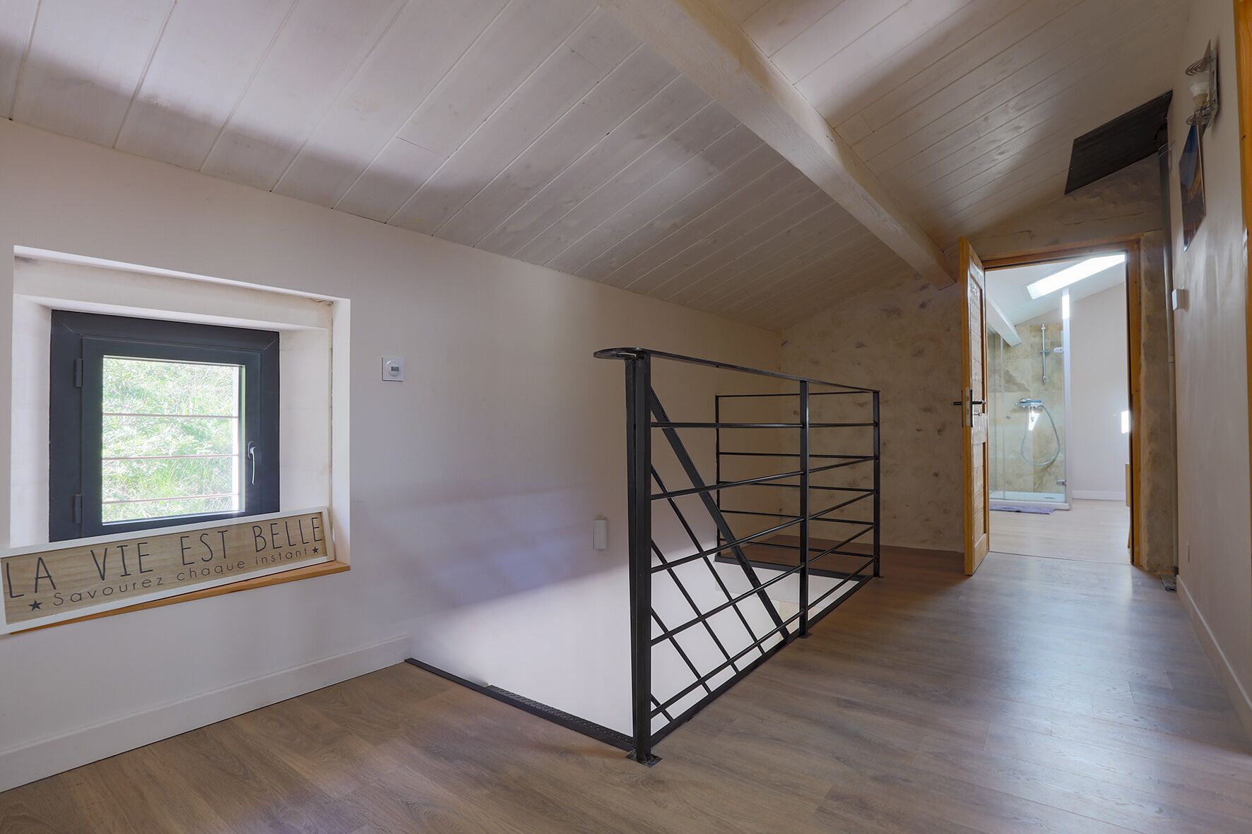 A room with a wooden floor, a window with a black frame, and a metal staircase railing.