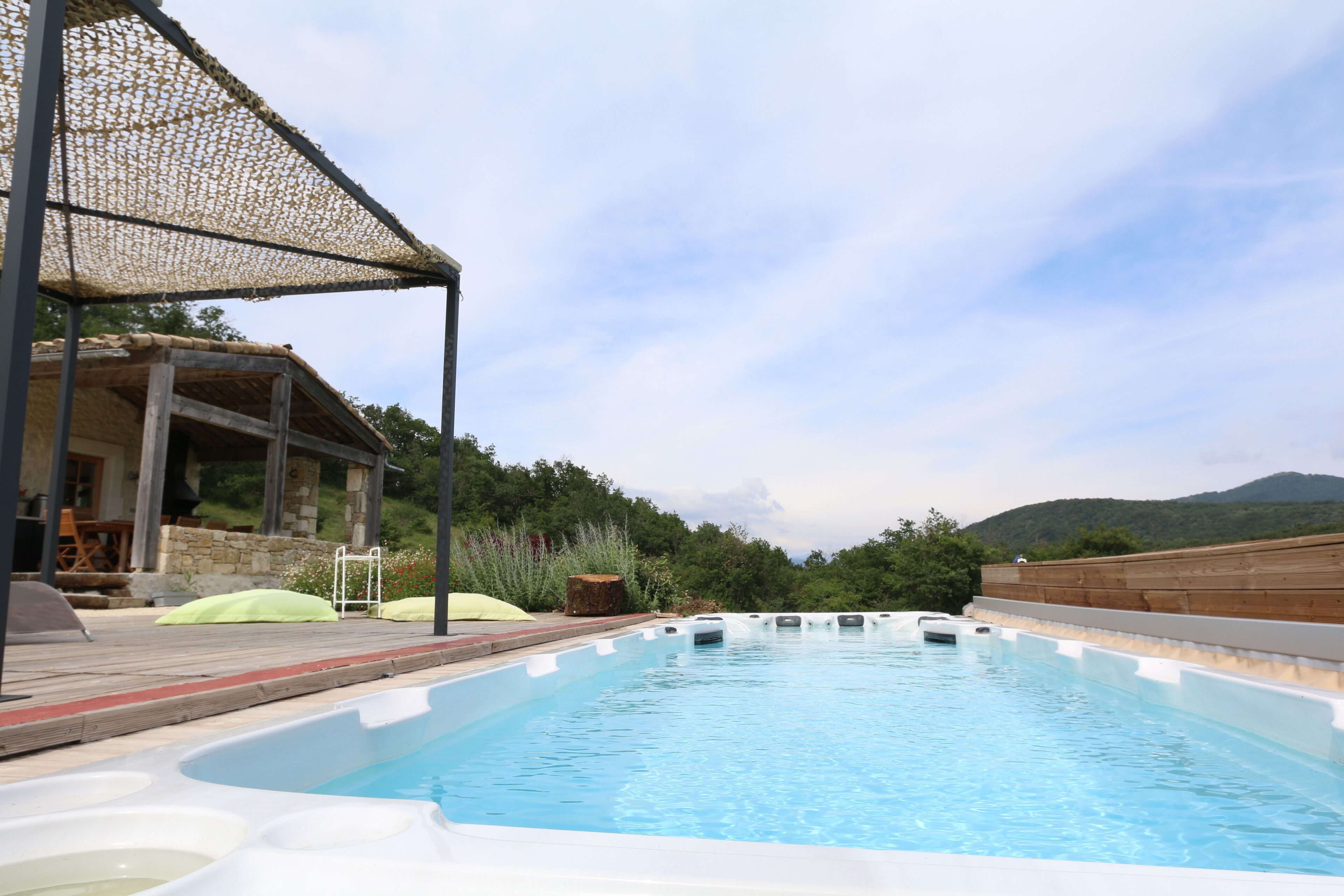 A swimming pool with a wooden deck, a covered seating area, and a view of hills in the background.