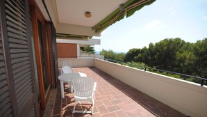 Un balcon avec une table et des chaises, une vue sur les arbres et un bâtiment à la façade en briques.