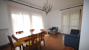 Un coin repas avec une table et des chaises en bois, une petite table ronde avec un pied blanc et un canapé bleu à motifs.