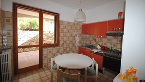 Une cuisine avec une table ronde et des chaises, des placards rouges, une cuisinière et, par une porte vitrée, une vue sur un espace extérieur.