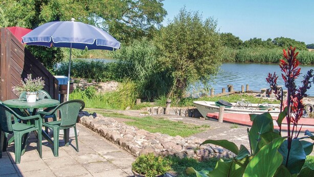 En terrasse med et bord og stole, en blå parasol og en båd ved vandet.