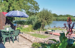 A patio with a table and chairs, a blue umbrella, and a boat docked by the water. - Lovely home in Usedom with house sea view (Usedom)
