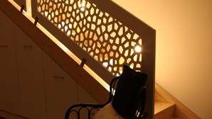 Una escalera con barandilla de diseño geométrico, una silla de metal negro con cojín estampado, y un piso de madera.