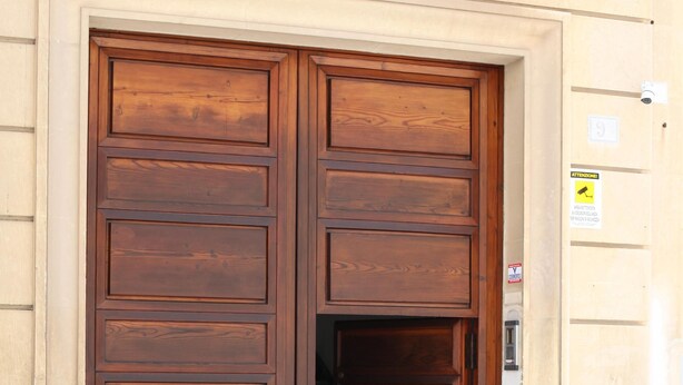 Una gran puerta doble de madera con un picaporte metálico, ubicada en un edificio de piedra con un escalón que la precede.