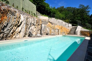 A swimming pool with a stone wall and stairs leading up to a building.