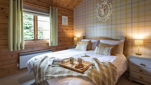 A cozy wooden room with a bed, bedside lamps, a window with curtains, and a decorative mirror on the wall. - Curlew Lodge - sleeps 6 guests  in 3 bedrooms (Ravenstonedale / Kirkby Stephen)