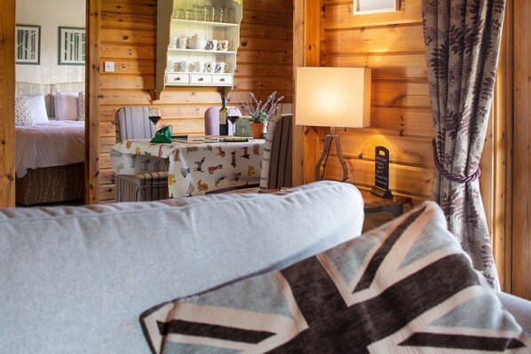 A cozy room with a bed, a table with a lamp, and a shelf with kitchenware.
