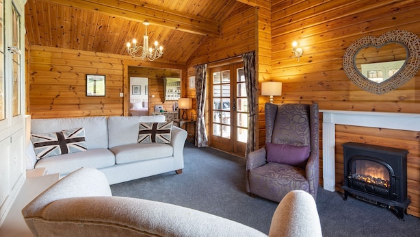 A cozy log cabin interior with a fireplace, a sofa, a chair, and a wooden ceiling. - Curlew Lodge - sleeps 6 guests  in 3 bedrooms (Ravenstonedale / Kirkby Stephen)