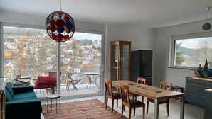 A modern living space with a dining area, a sofa, a patterned rug, and a view of a snowy town through large windows. - Warm magic in the heart of the Black Forest (Titisee-Neustadt)