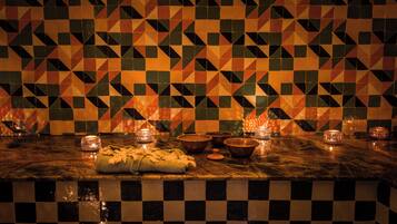 Un mur recouvert de carreaux aux motifs géométriques et un comptoir en marbre agrémenté de bougies et de bols.