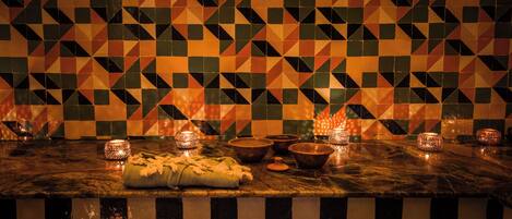A checkered tiled wall with geometric patterns and a marble countertop with candles and bowls.
