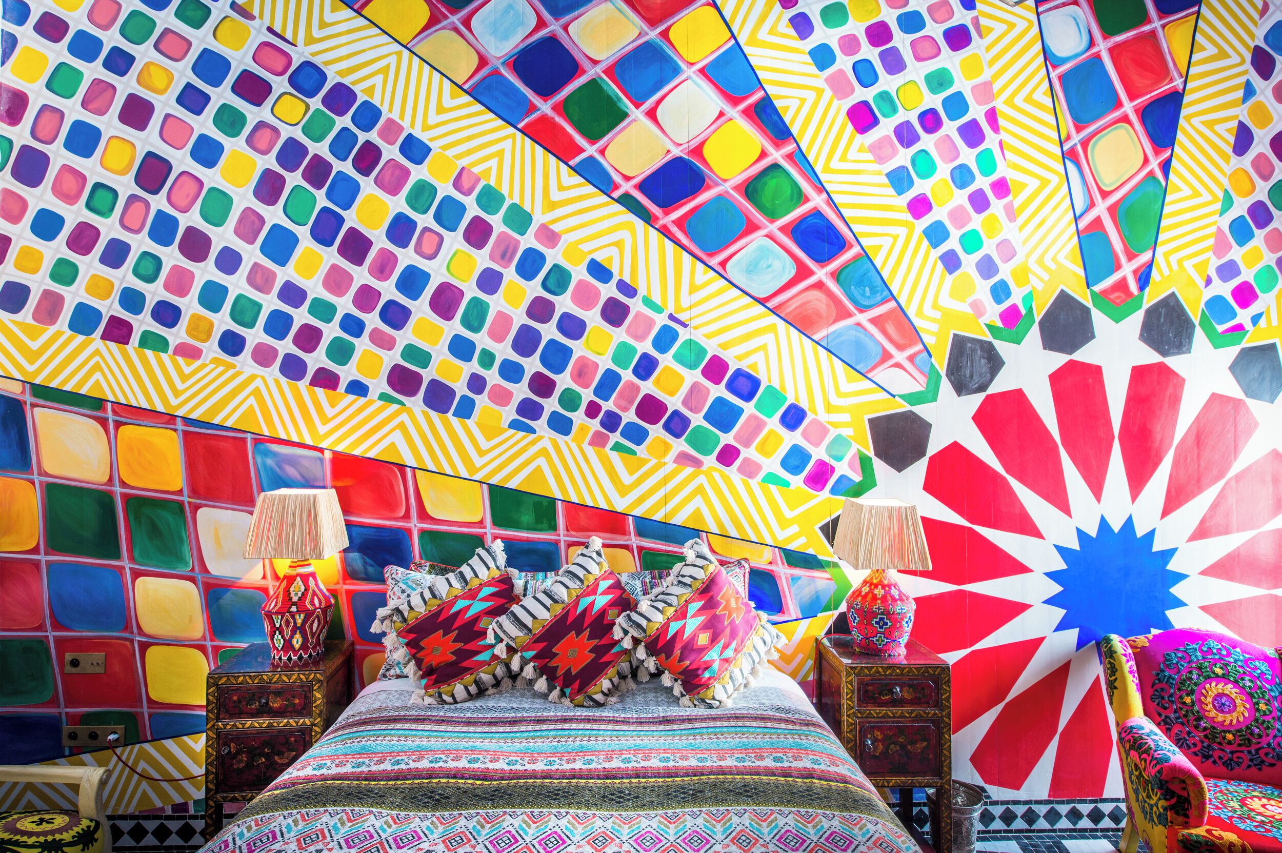 A vibrant room with a colorful mosaic wall, a patterned bedspread, and decorative pillows.