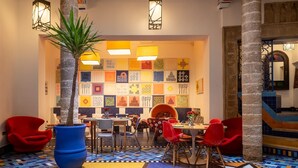 Un coin repas avec un sol carrelé aux couleurs vives, une table centrale entourée de chaises et une grande plante en pot.
