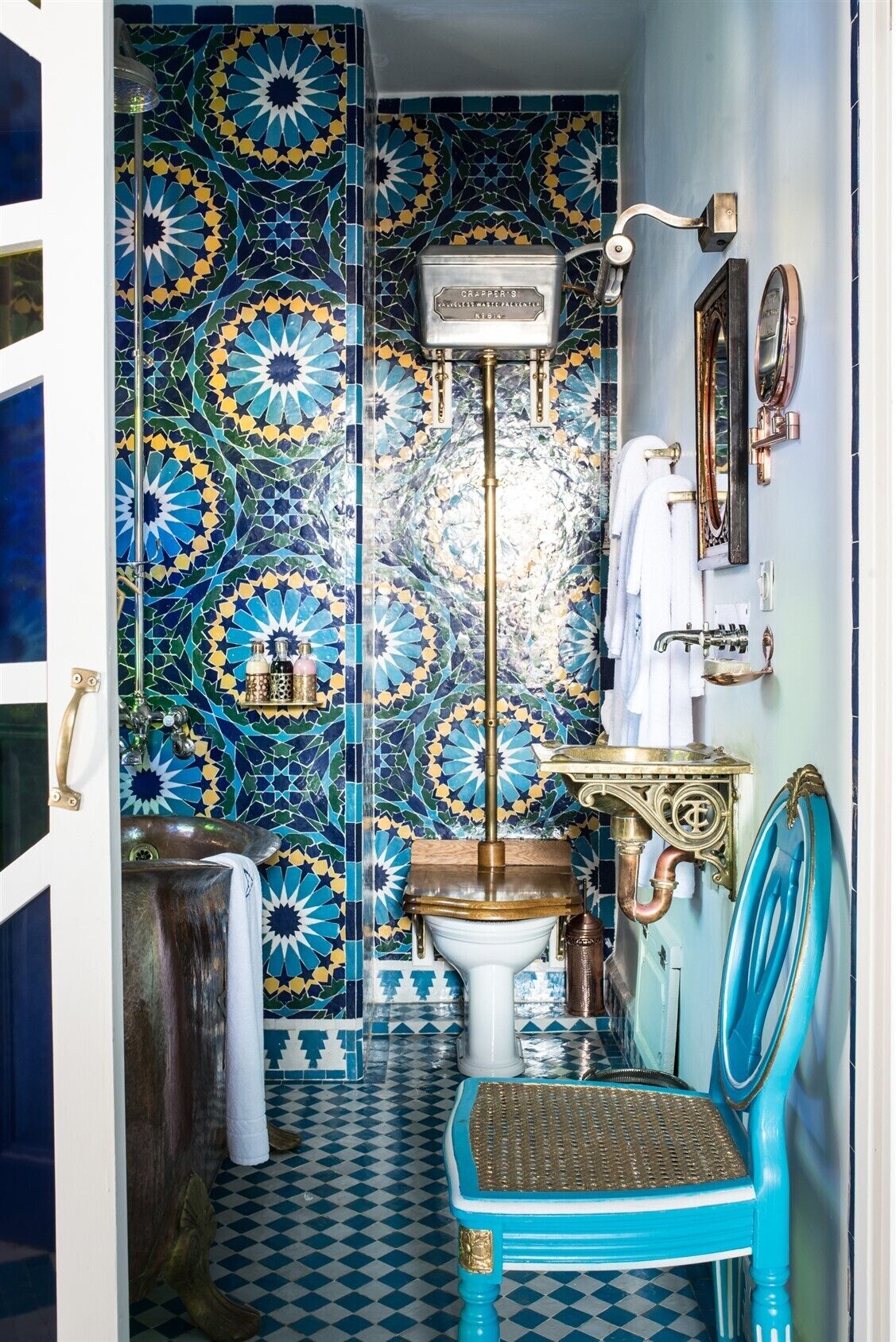 A bathroom with a patterned tile wall, a white sink, a blue chair, and a towel rack.