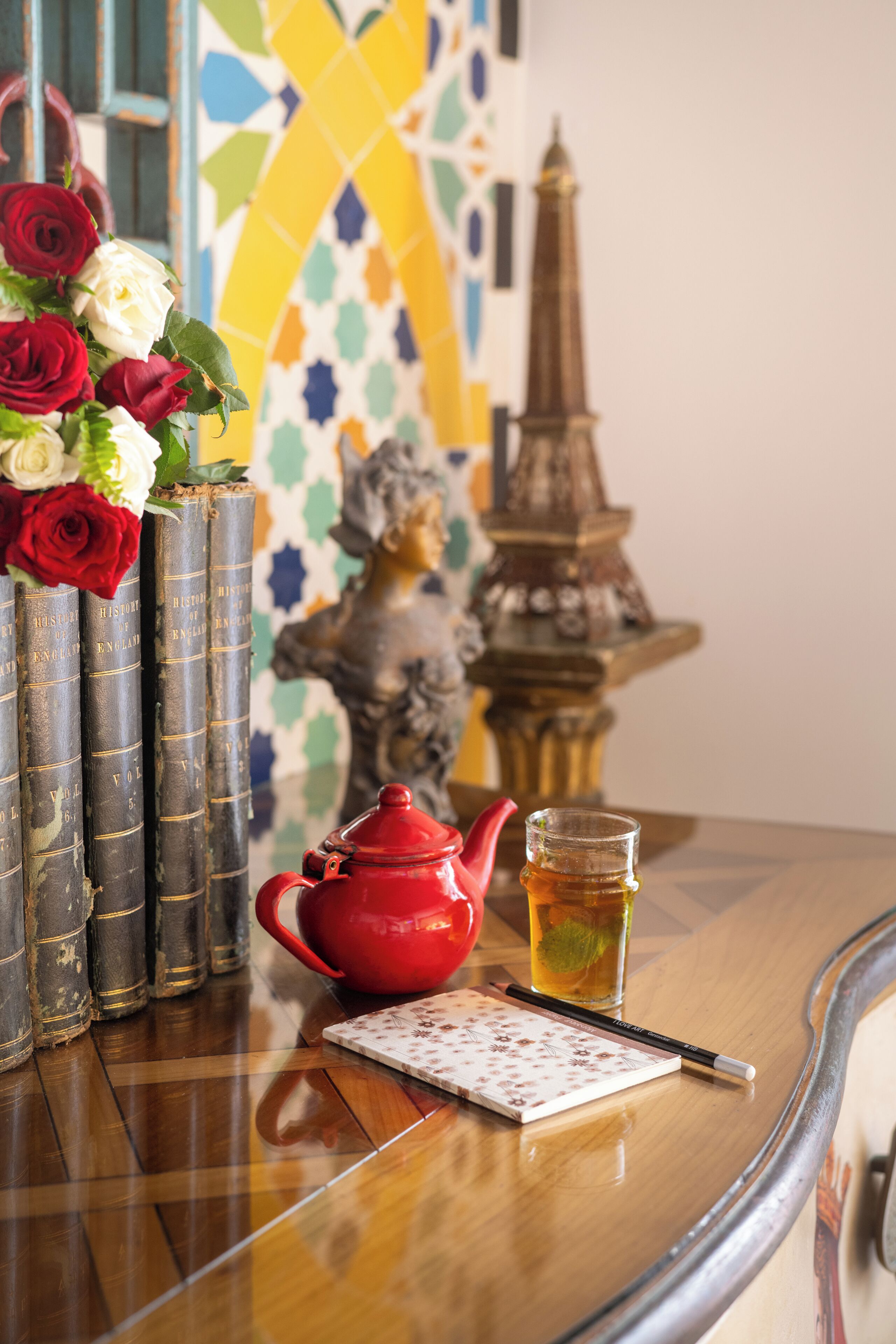 Una mesa con una tetera, una taza de té, un cuaderno y un jarrón de rosas.