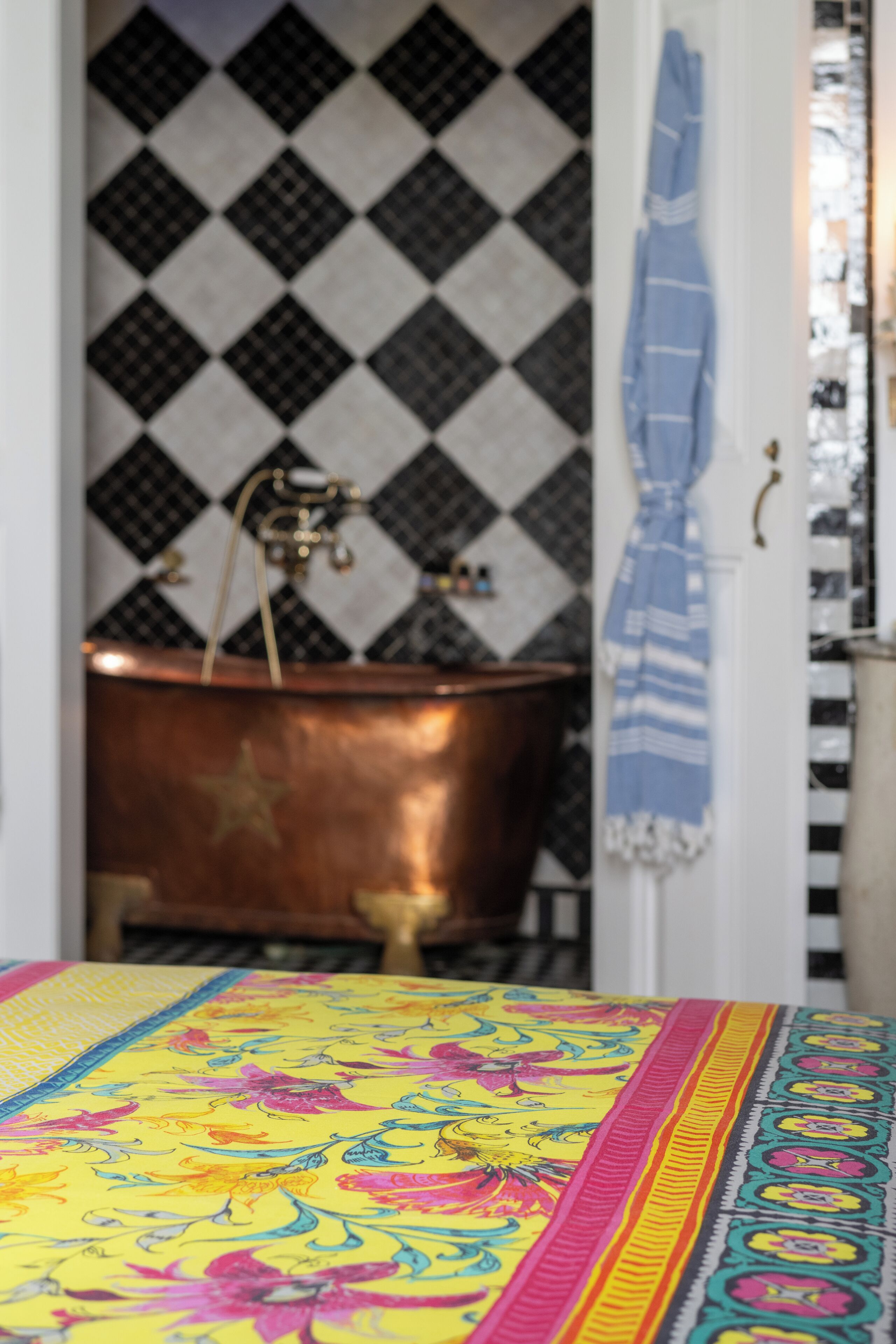 A bathroom with a copper bathtub, a patterned wall, and a striped towel hanging on the door.