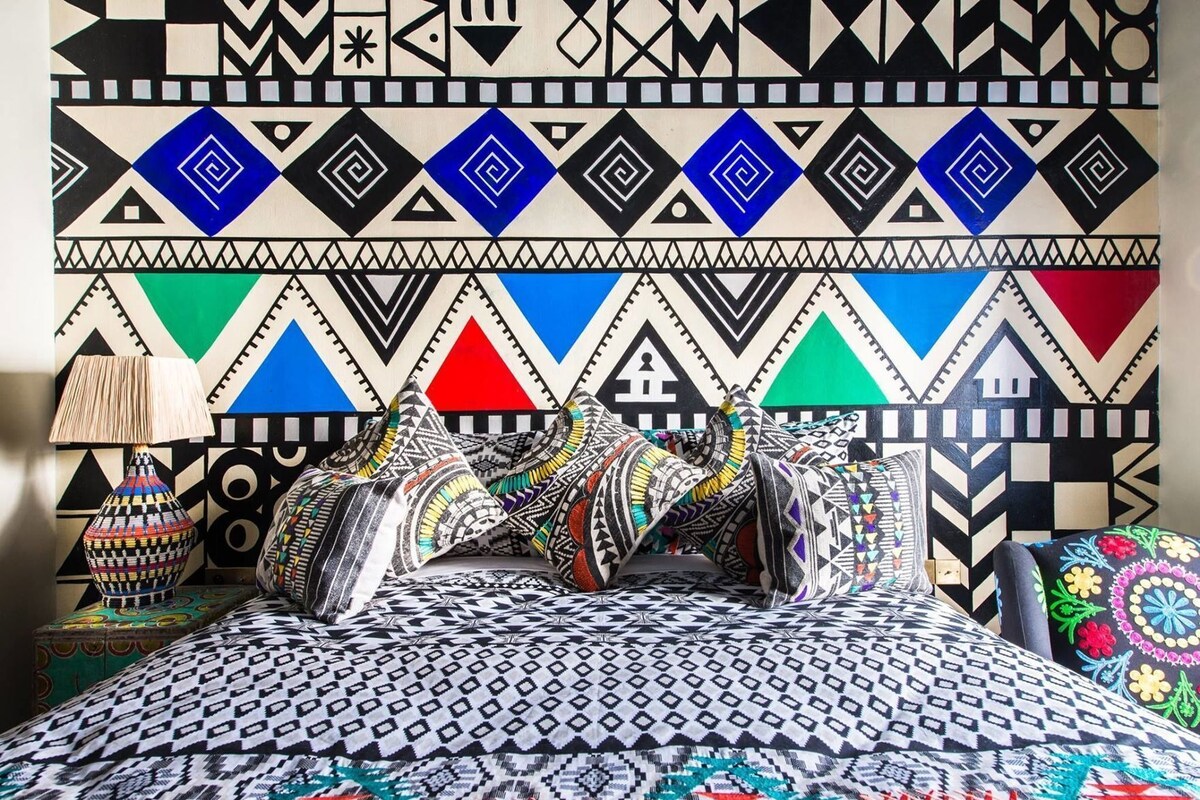Un lit avec une literie à motifs, des oreillers et un mur orné de motifs géométriques.