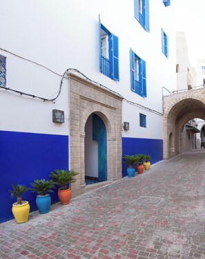 Une ruelle étroite pavée, bord ée de bâtiments blancs aux volets bleus et surmontée d’une arche en pierre.