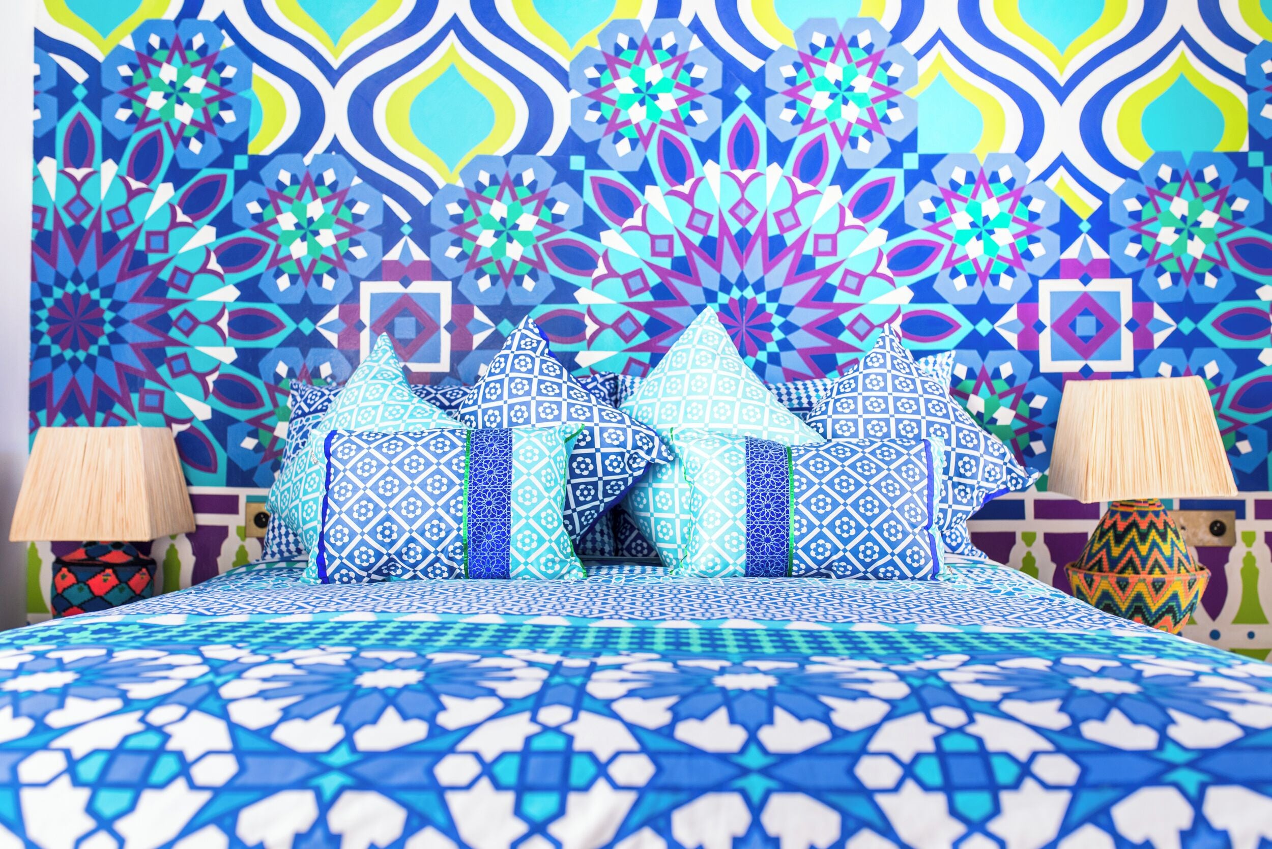 A bed with patterned bedding, pillows, and a wall with geometric designs.