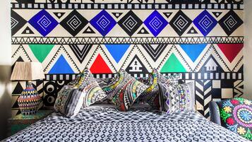 A bed with patterned bedding and pillows, a lamp, and a wall with geometric designs.