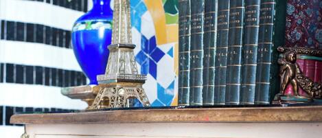 Un meuble décoratif orné d’une figure royale peinte, un vase bleu rempli de fleurs et une pile de livres.