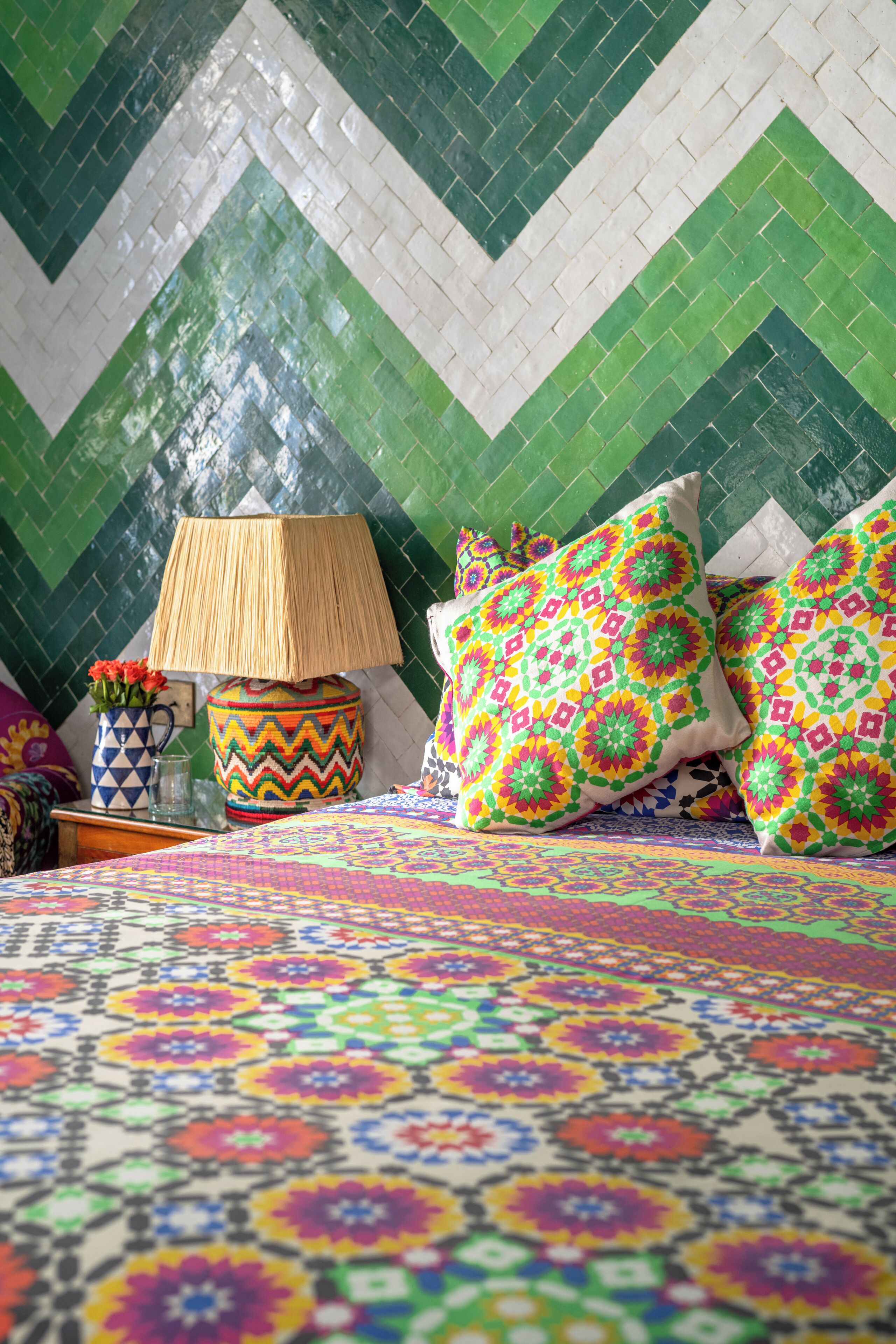 A bed with a colorful patterned bedspread, a woven lamp, and decorative pillows with geometric patterns.