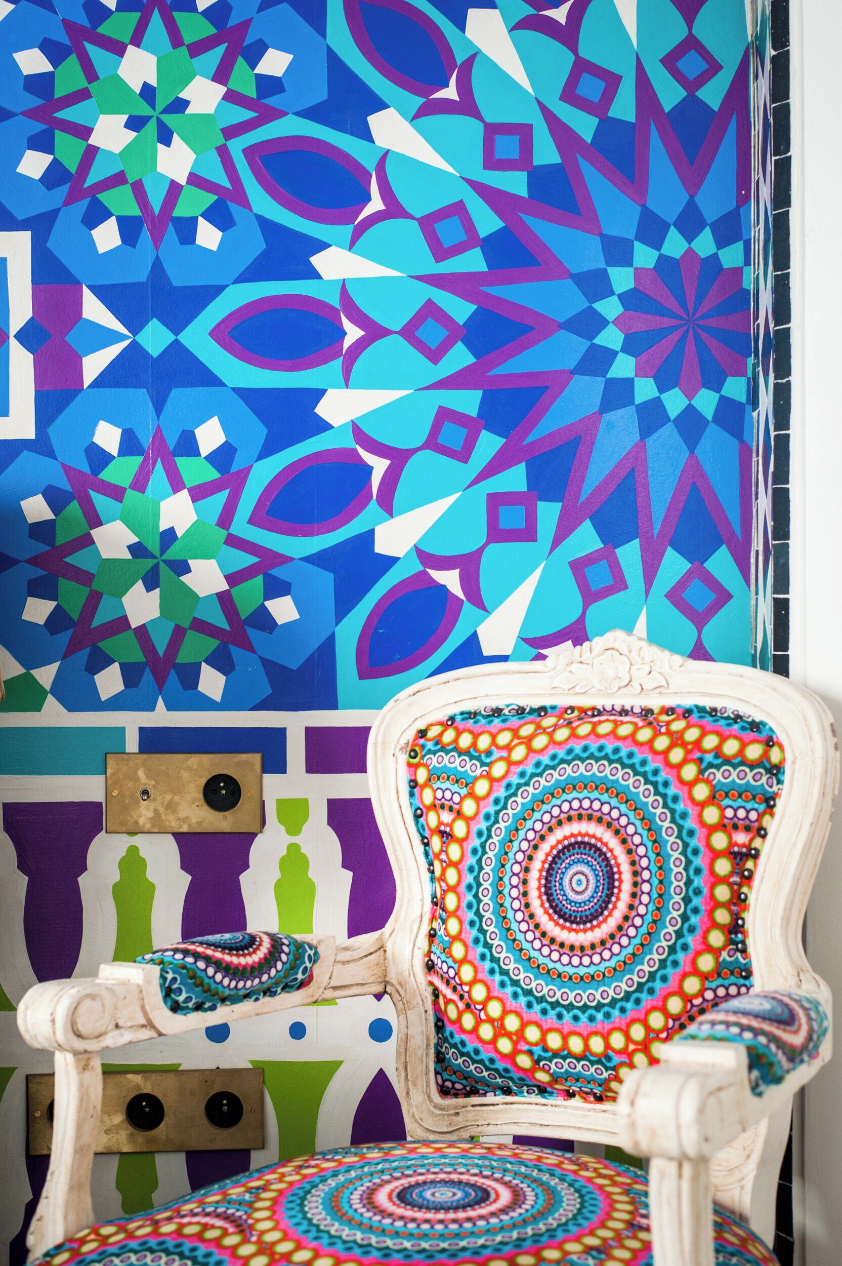 A chair with a colorful, patterned cushion and a geometric wall design in the background.