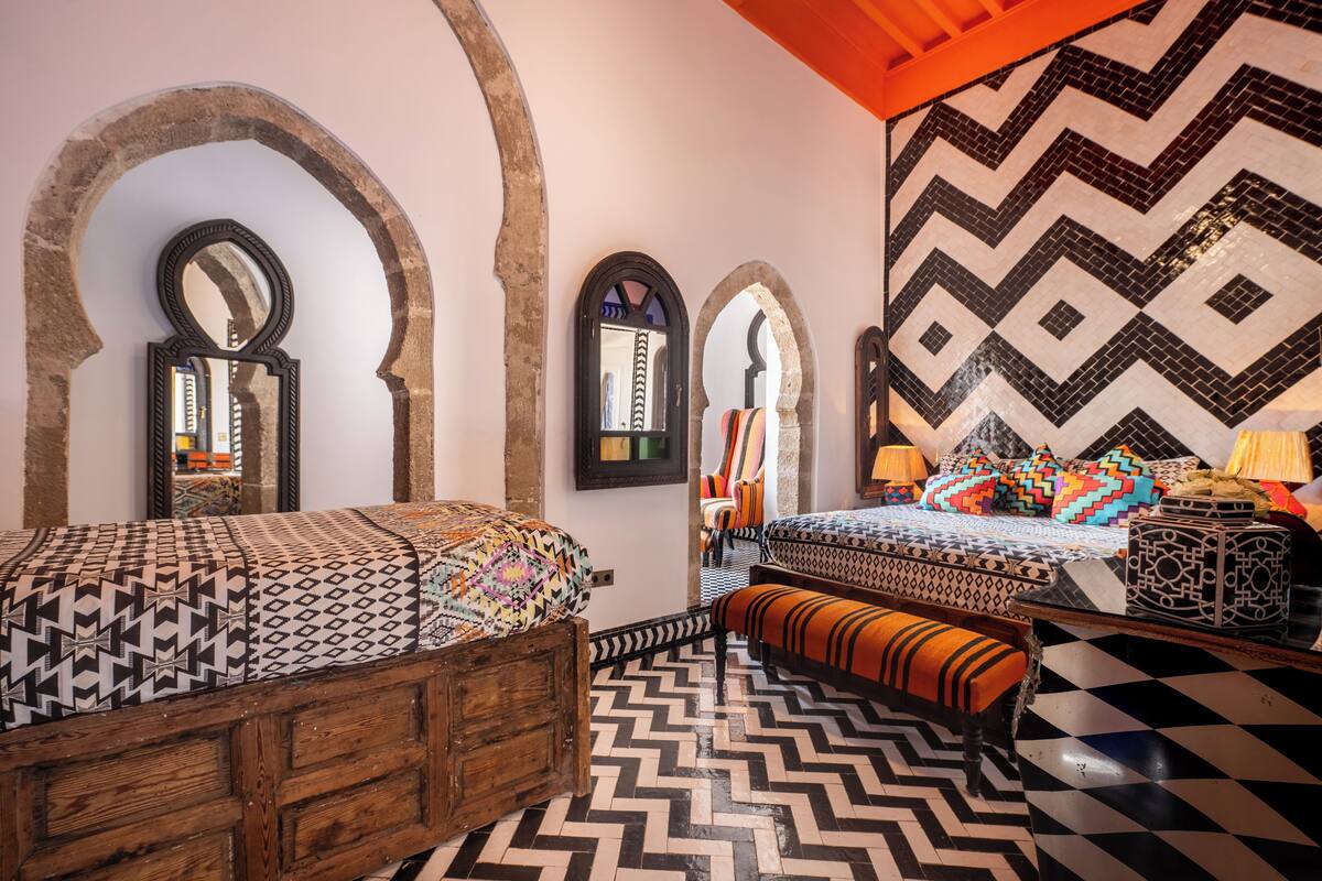 Une chambre avec deux lits, des têtes de lit en bois et un sol à motifs.