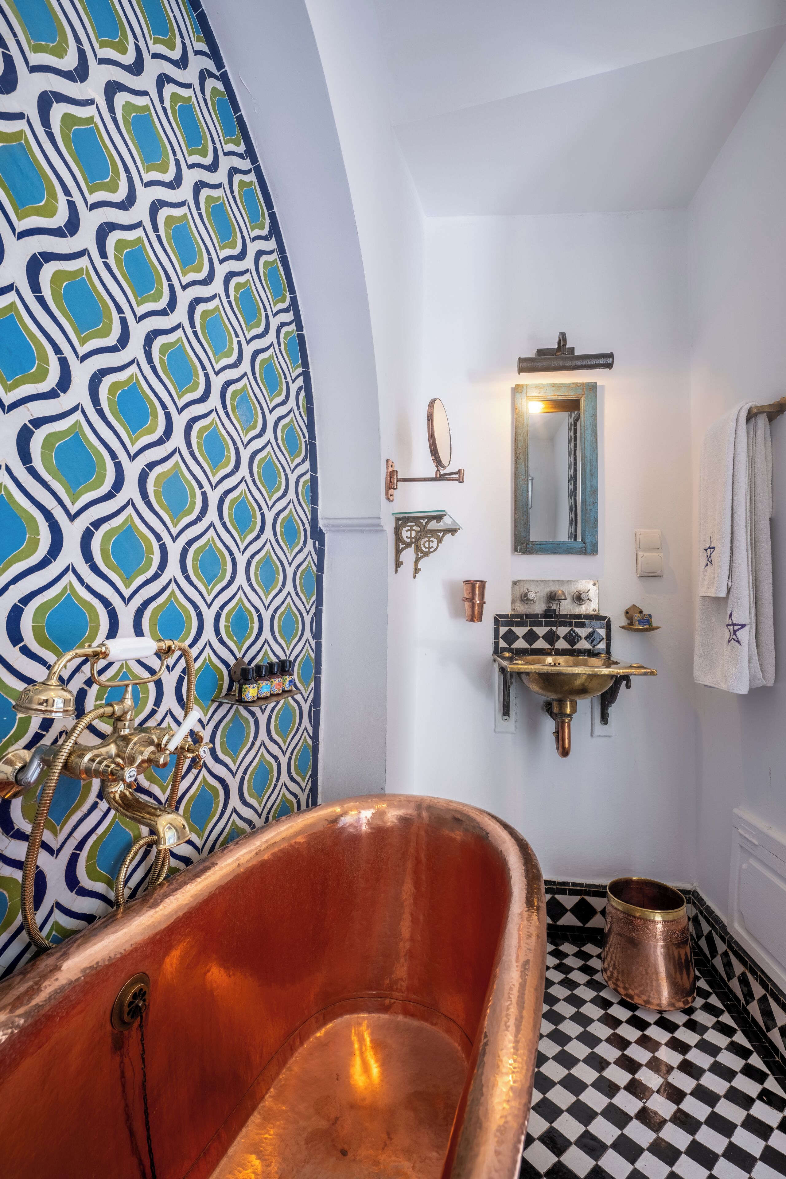 A bathroom with a copper bathtub, a patterned wall, a sink with a mirror, and a checkered floor.
