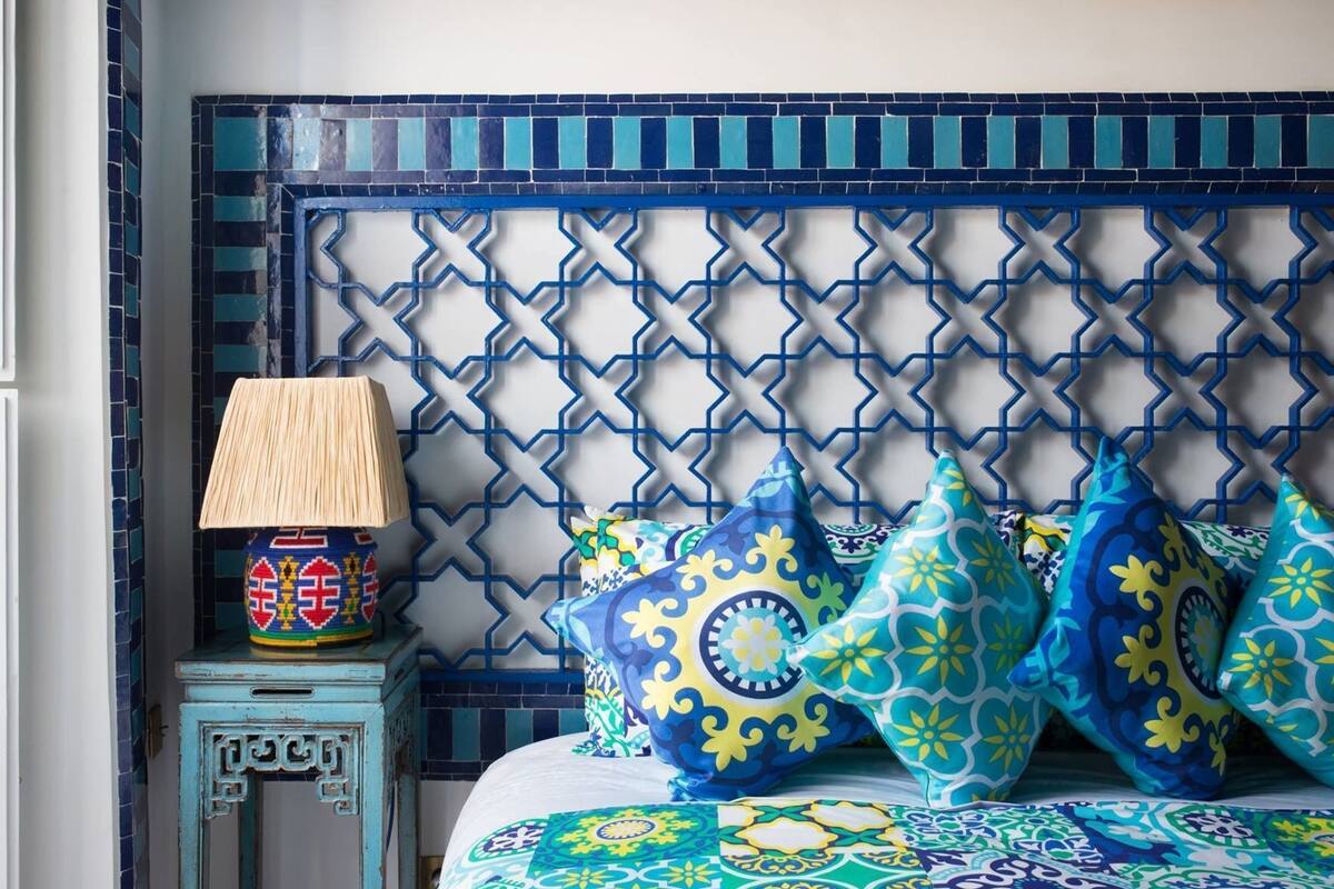 Un lit avec des coussins à motifs, une lampe de chevet et un panneau décoratif mural.