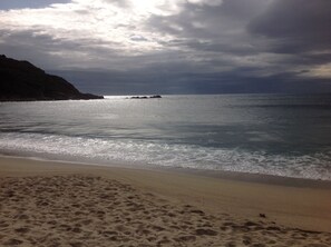 En strand med en sandstrand och ett lugnt hav under en molnig himmel.