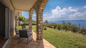 Un portico coperto con un arco in pietra, un tavolo con sedie e vista sul mare e sulle montagne.