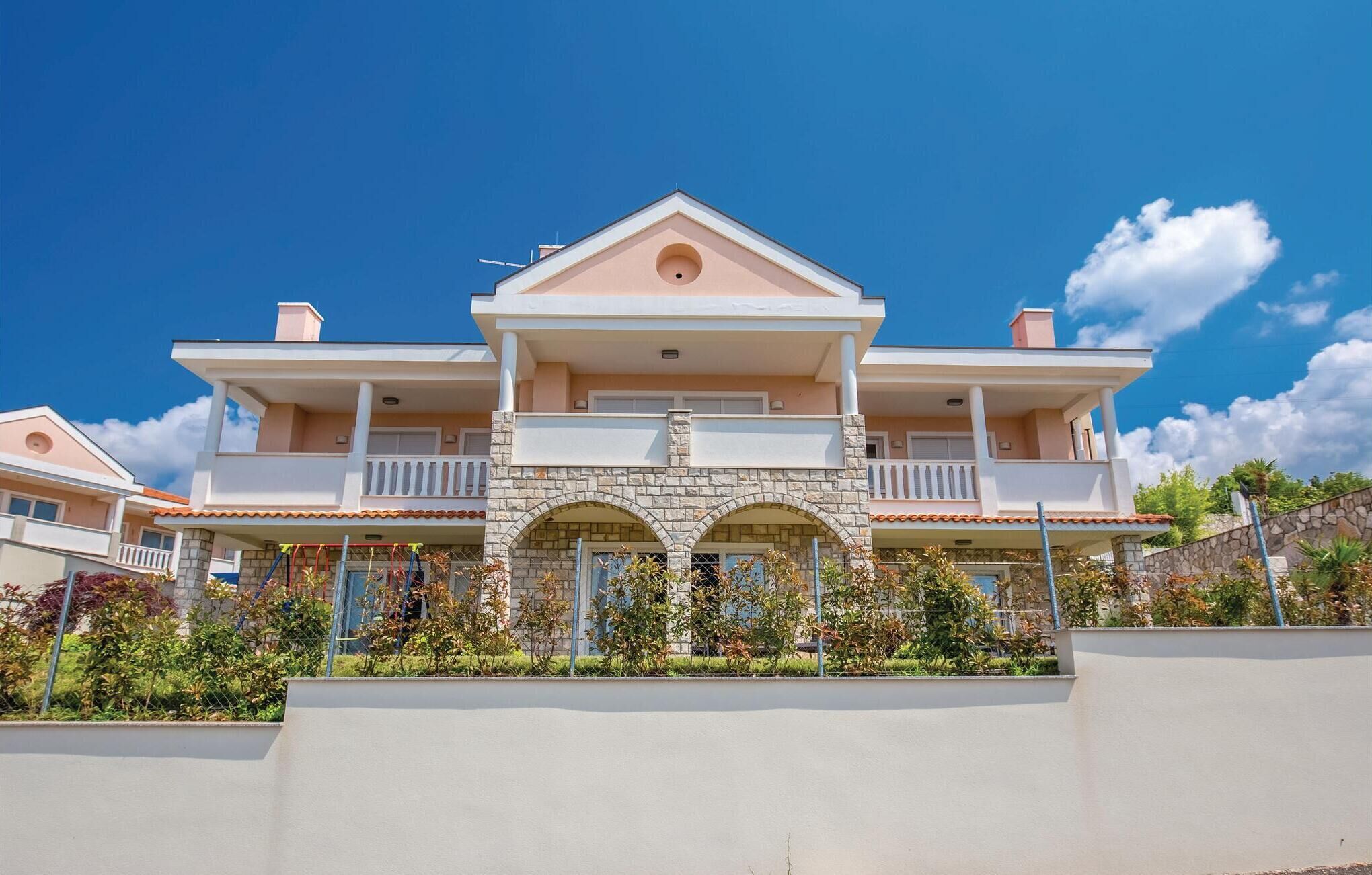 A two-story house with a balcony, a stone archway, and a clear blue sky.